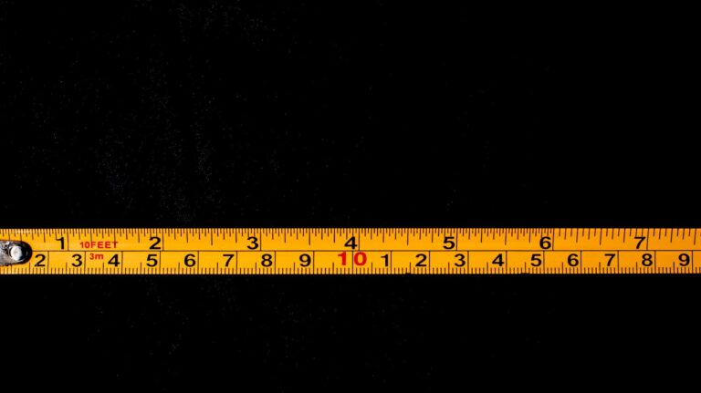 A close-up of a yellow tape measure laid out on a black background.