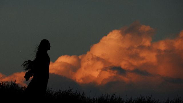Silhouette of a woman against a vibrant sunset sky with dramatic clouds, creating a striking scene.